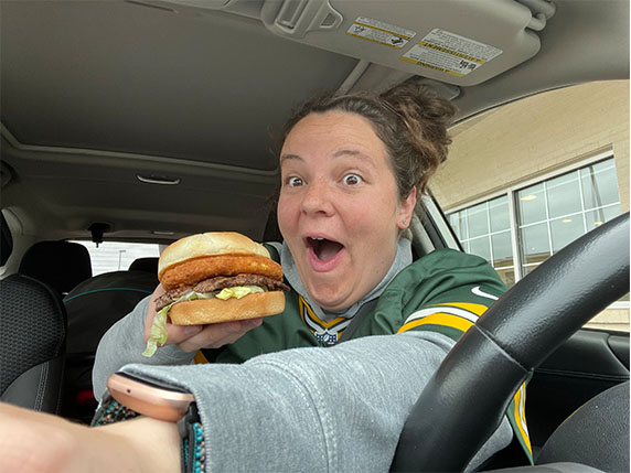 A woman in a car smiles in amazement holding her CurderBurger.